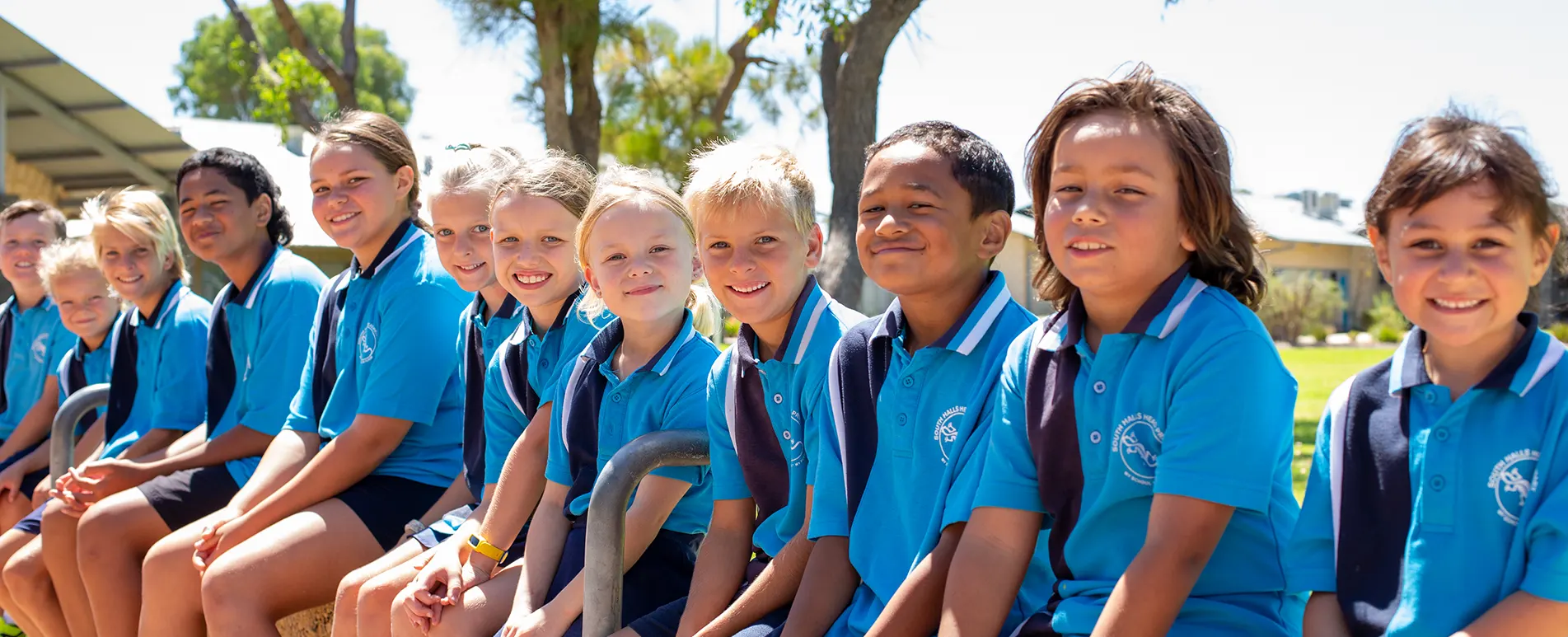A row of smiling South Halls Head students sitting together outdoors in school uniform